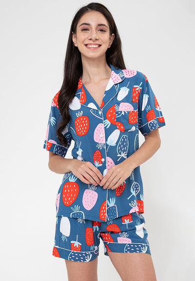A woman standing and wearing a short sleeve shorts set with a strawberry print design