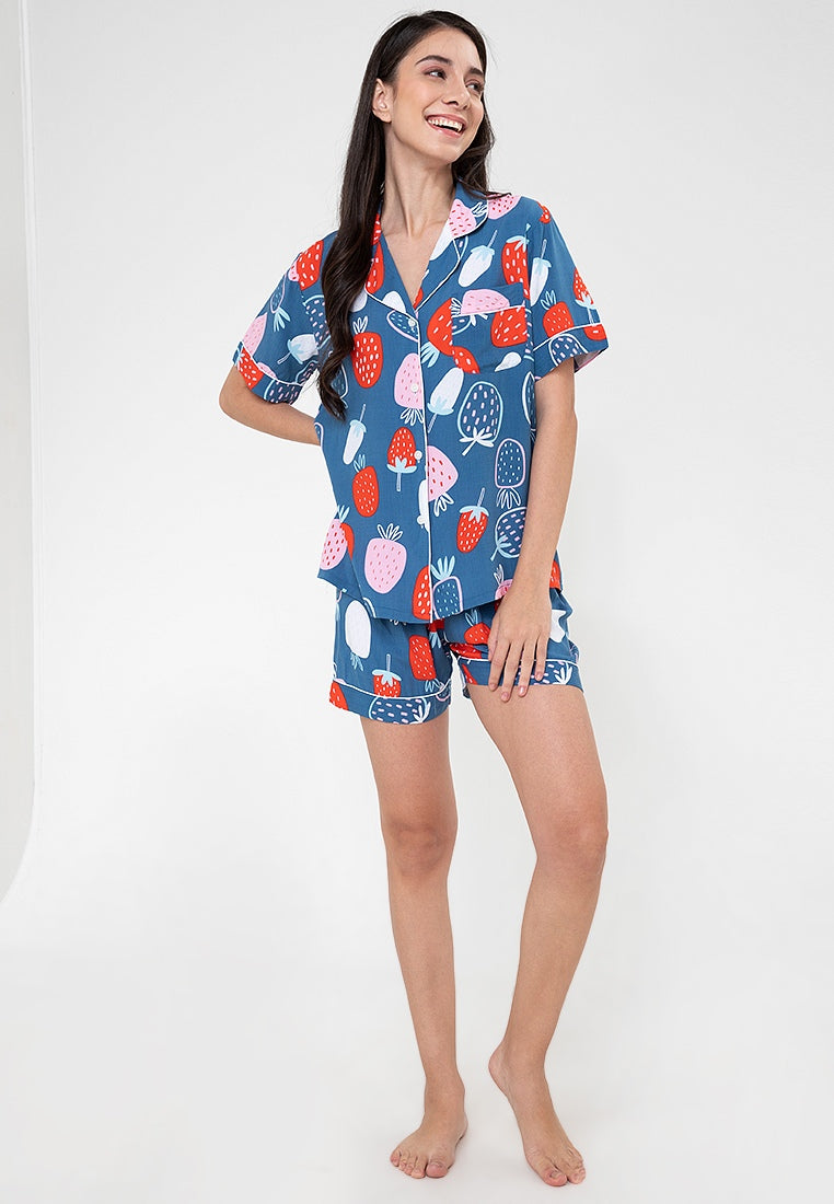 A woman standing and wearing a short sleeve shorts set with a strawberry print design