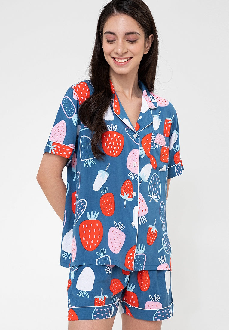 A woman standing and wearing a short sleeve shorts set with a strawberry print design