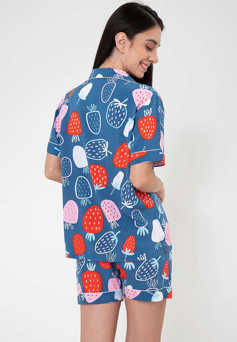 A woman standing and wearing a short sleeve shorts set with a strawberry print design