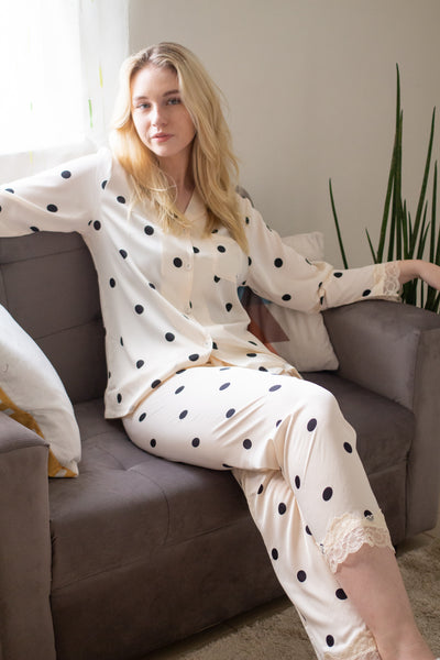 A woman sitting wearing a silk long sleeve pajama set with polka dot design