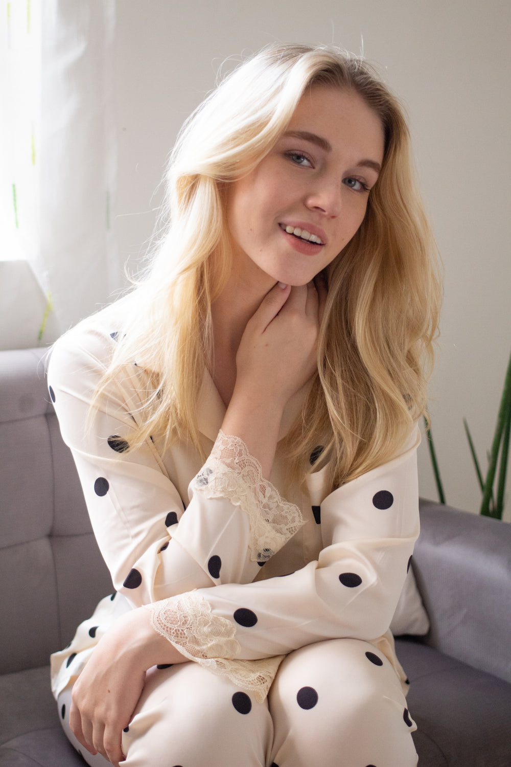 A woman sitting wearing a silk long sleeve pajama set with polka dot design