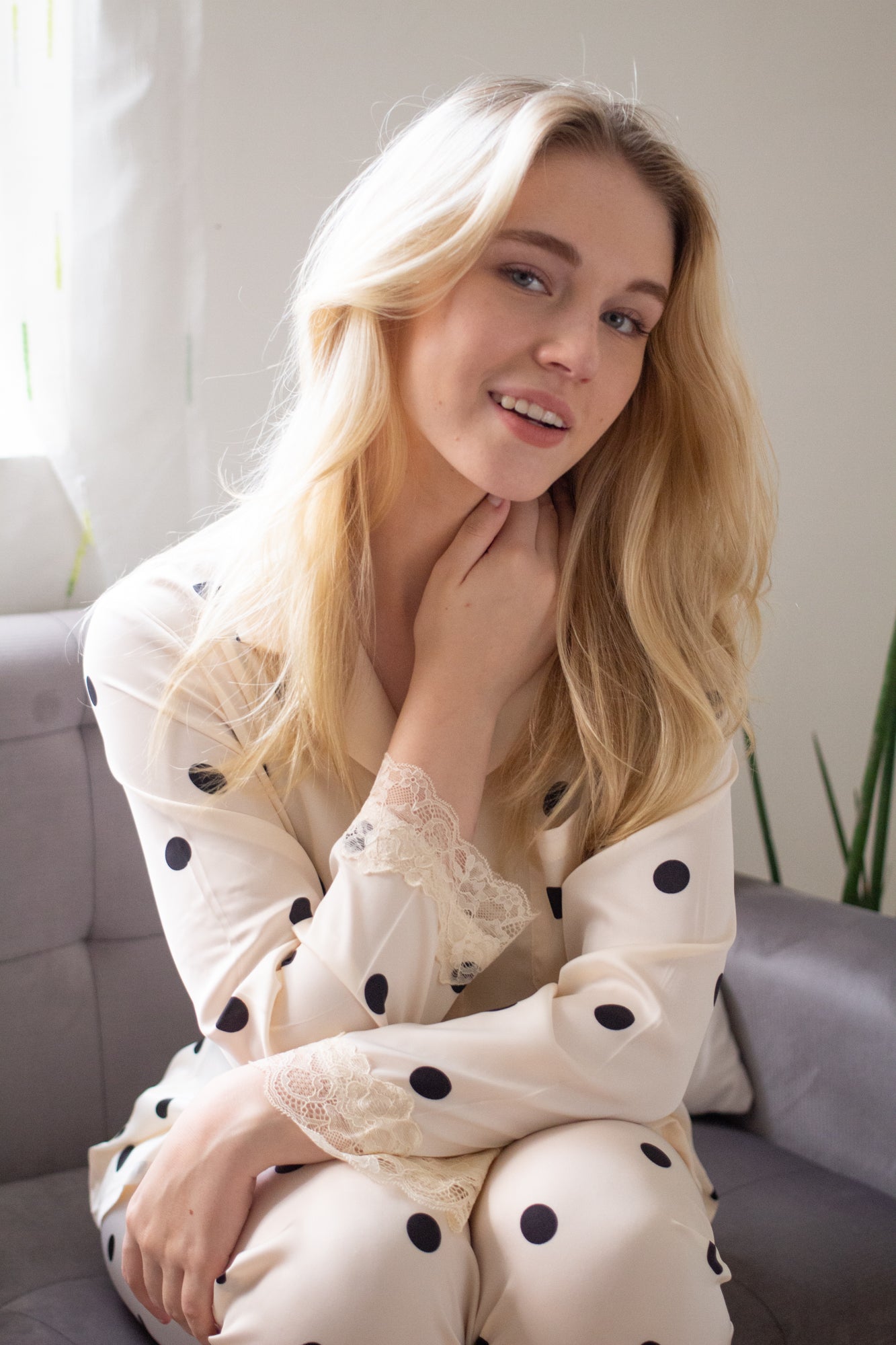 A woman sitting wearing a silk long sleeve pajama set with polka dot design