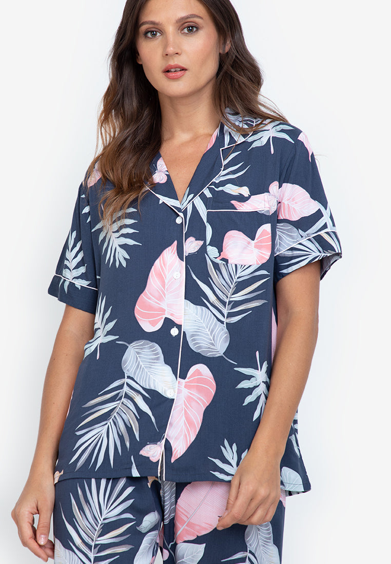 A woman standing and wearing a short sleeve pajama set in a tropical design