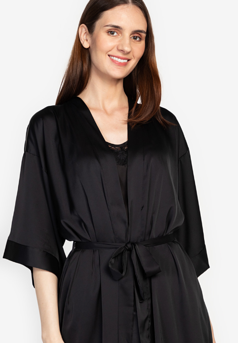 A woman standing and wearing a black Silk Romper set